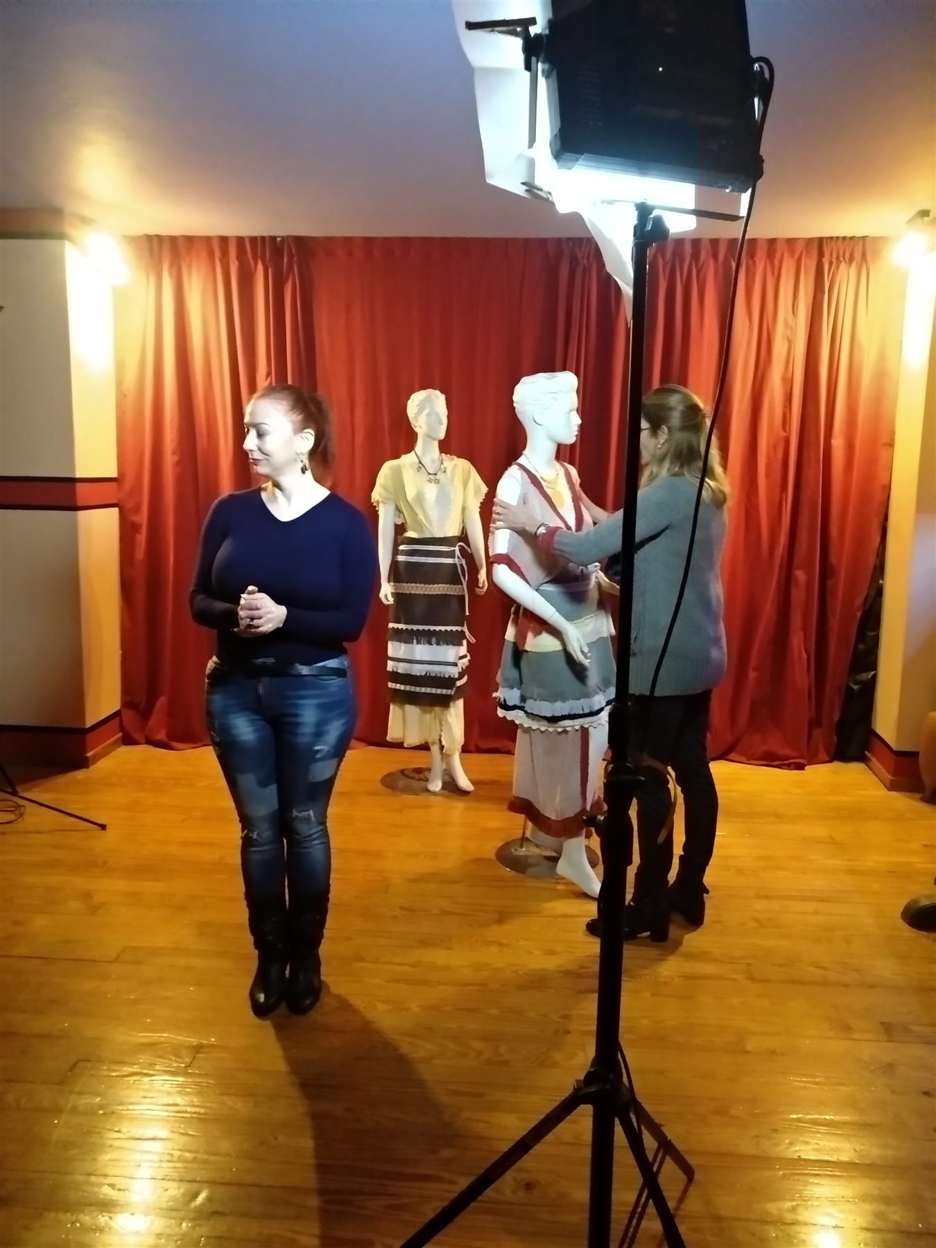 COSMOTE Ancient Greek Dress filming — 006 Presenter and another participant beside dressed mannequins under studio lighting