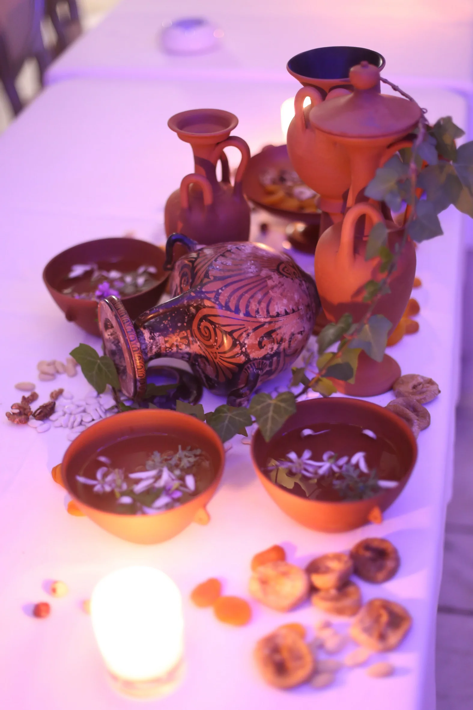 Reconstructed ceramic vessels, bowls, ivy and dried fruit arranged on the candlelit dinner table