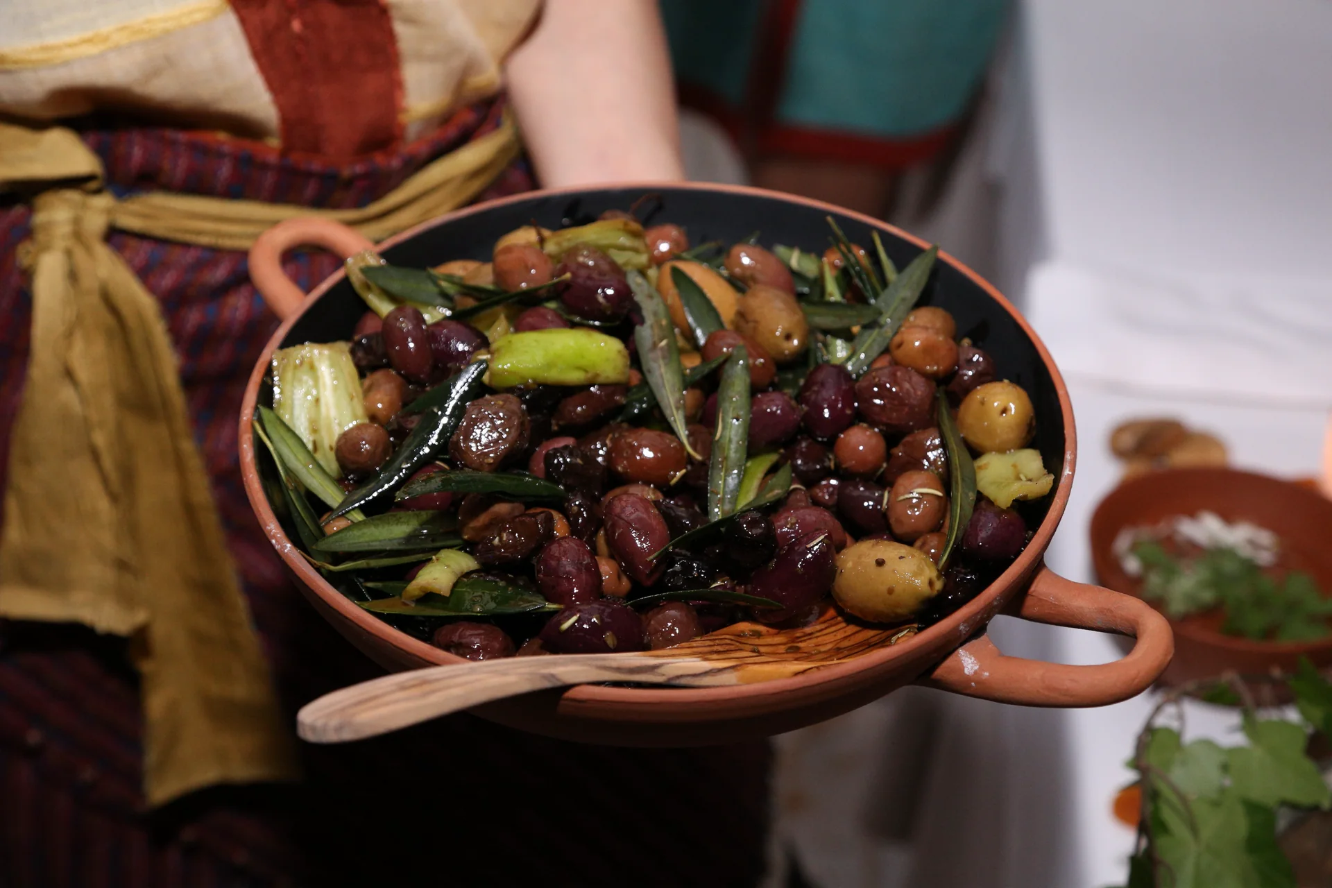 Mixed olives dressed with olive leaves and aromatics in a terracotta serving dish
