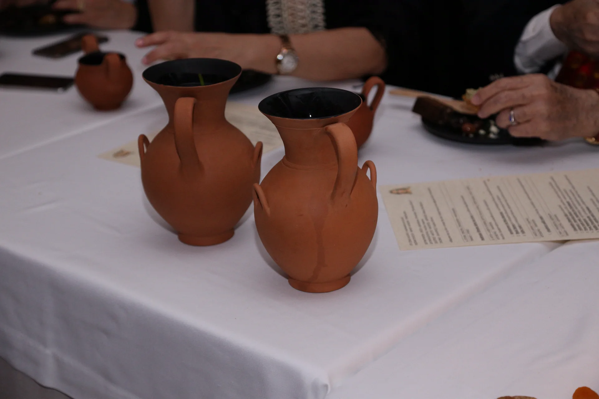 Two reconstructed terracotta jugs set among guests and printed menus