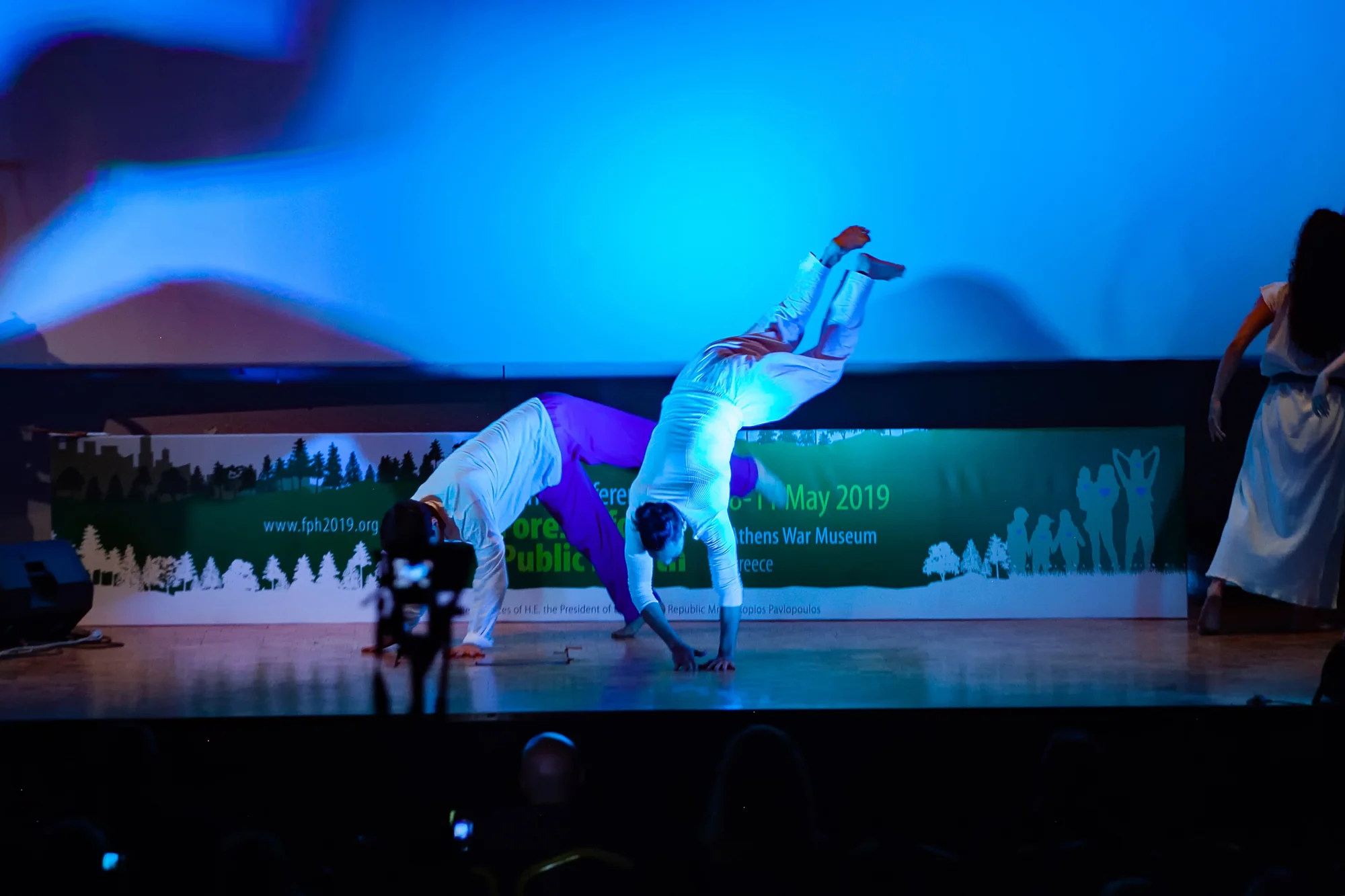 Two dancers balance on their hands in front of the World Conference on Forests for Public Health signage.
