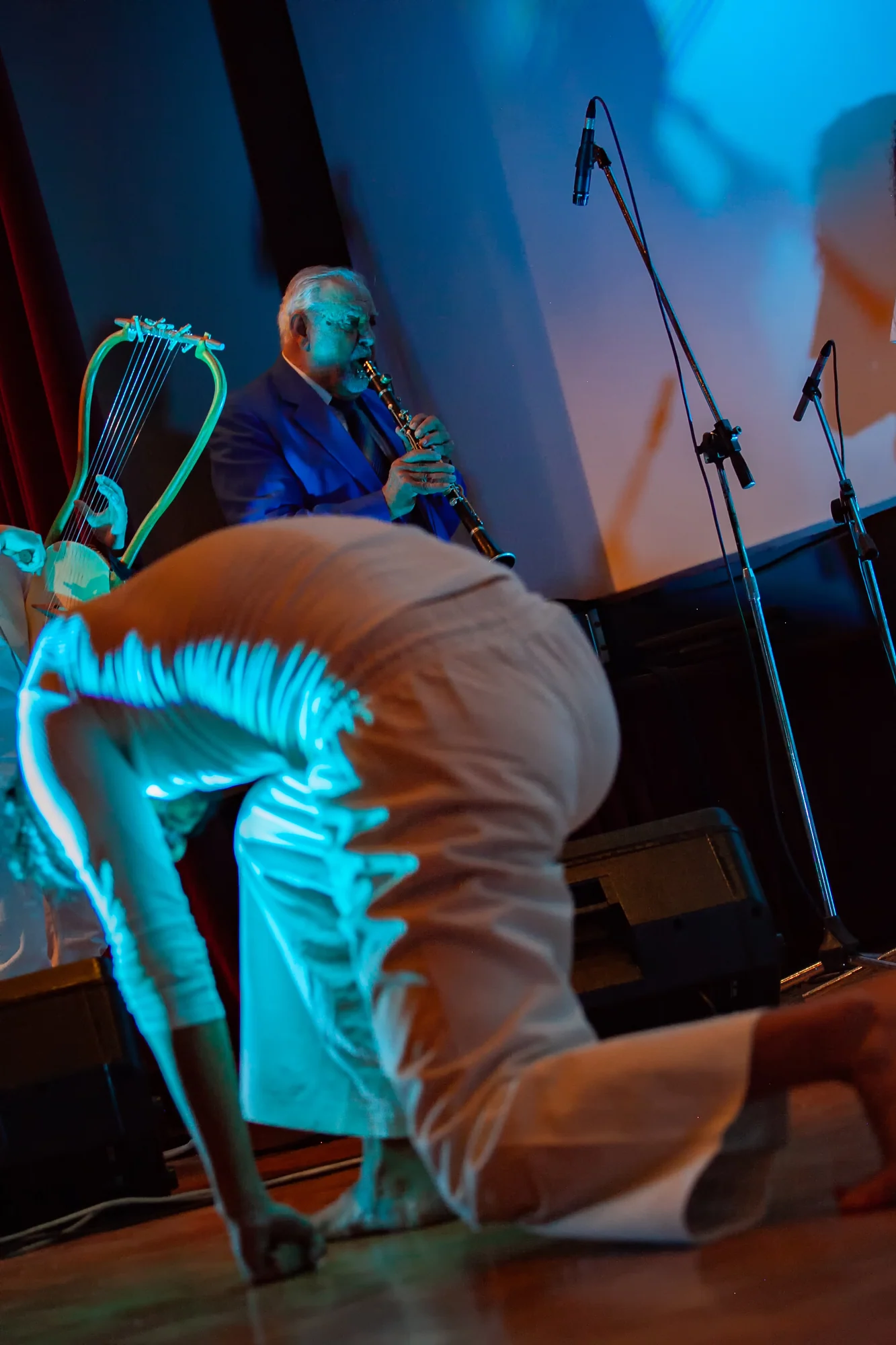 A dancer bends towards the stage floor, with a clarinettist and a lyre visible behind.