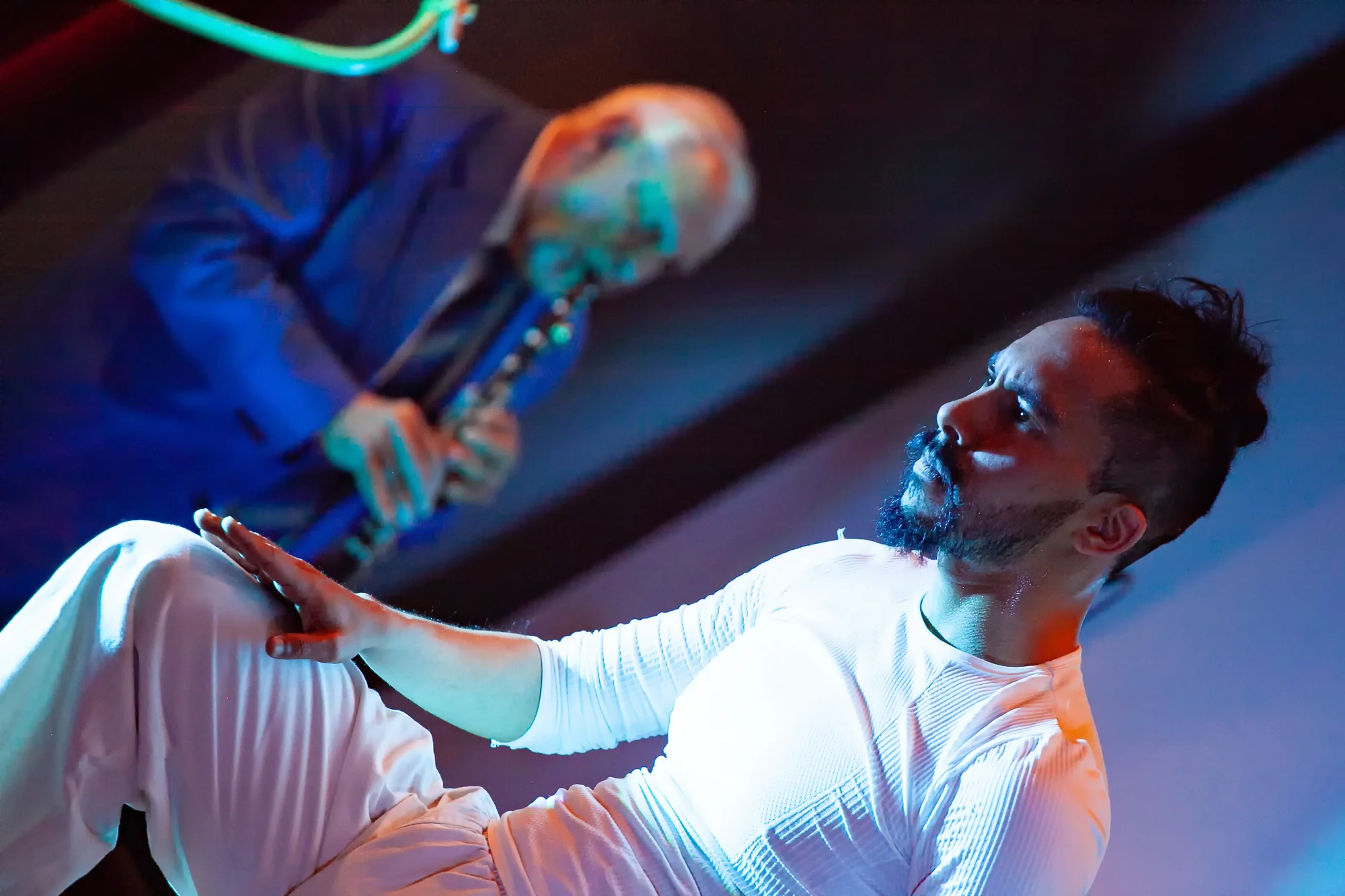 A dancer in white performs close to the floor while a clarinettist plays in the background.