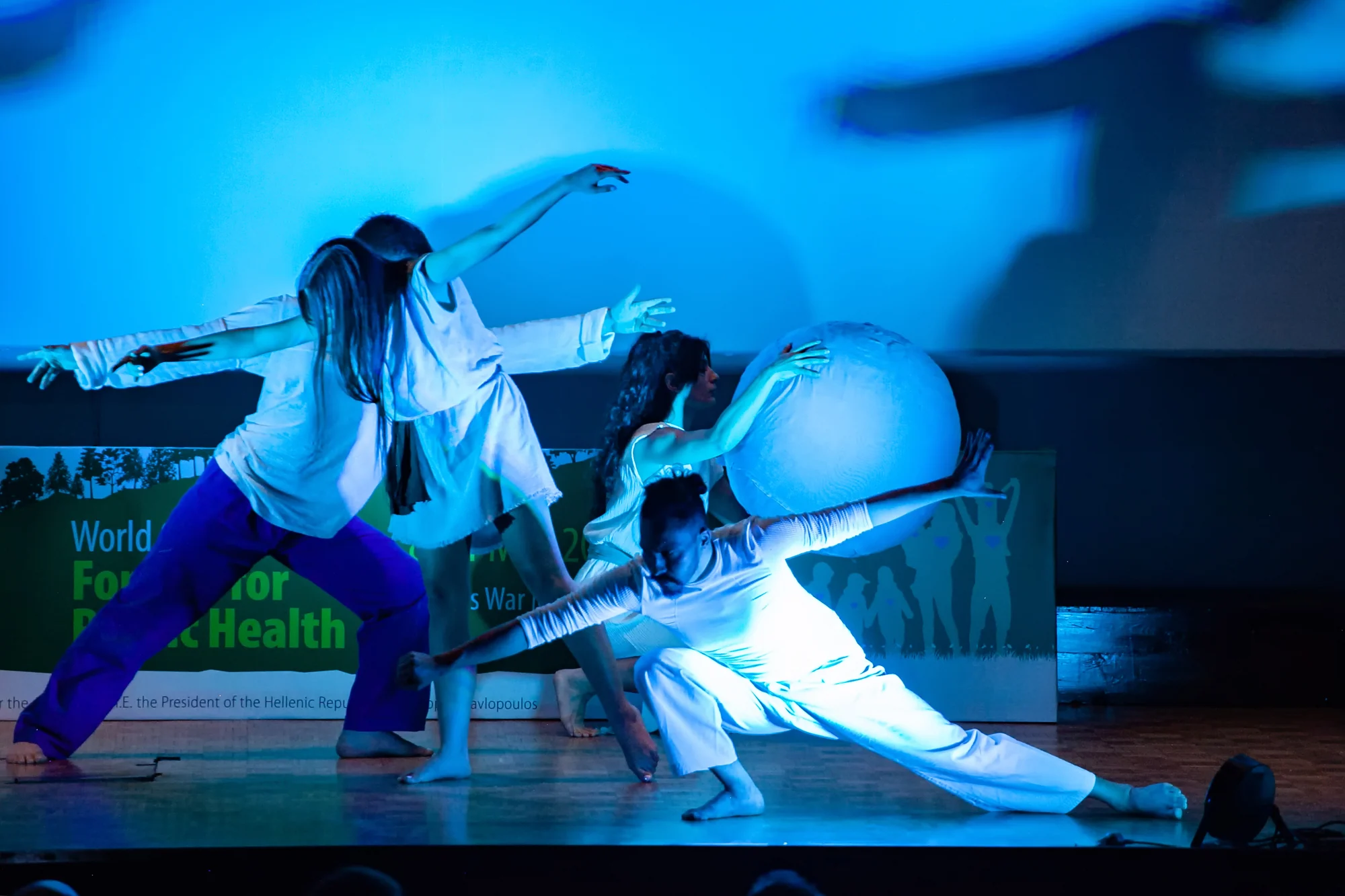 The dancers form an extended group composition around the globe, with one performer lunging near the floor.
