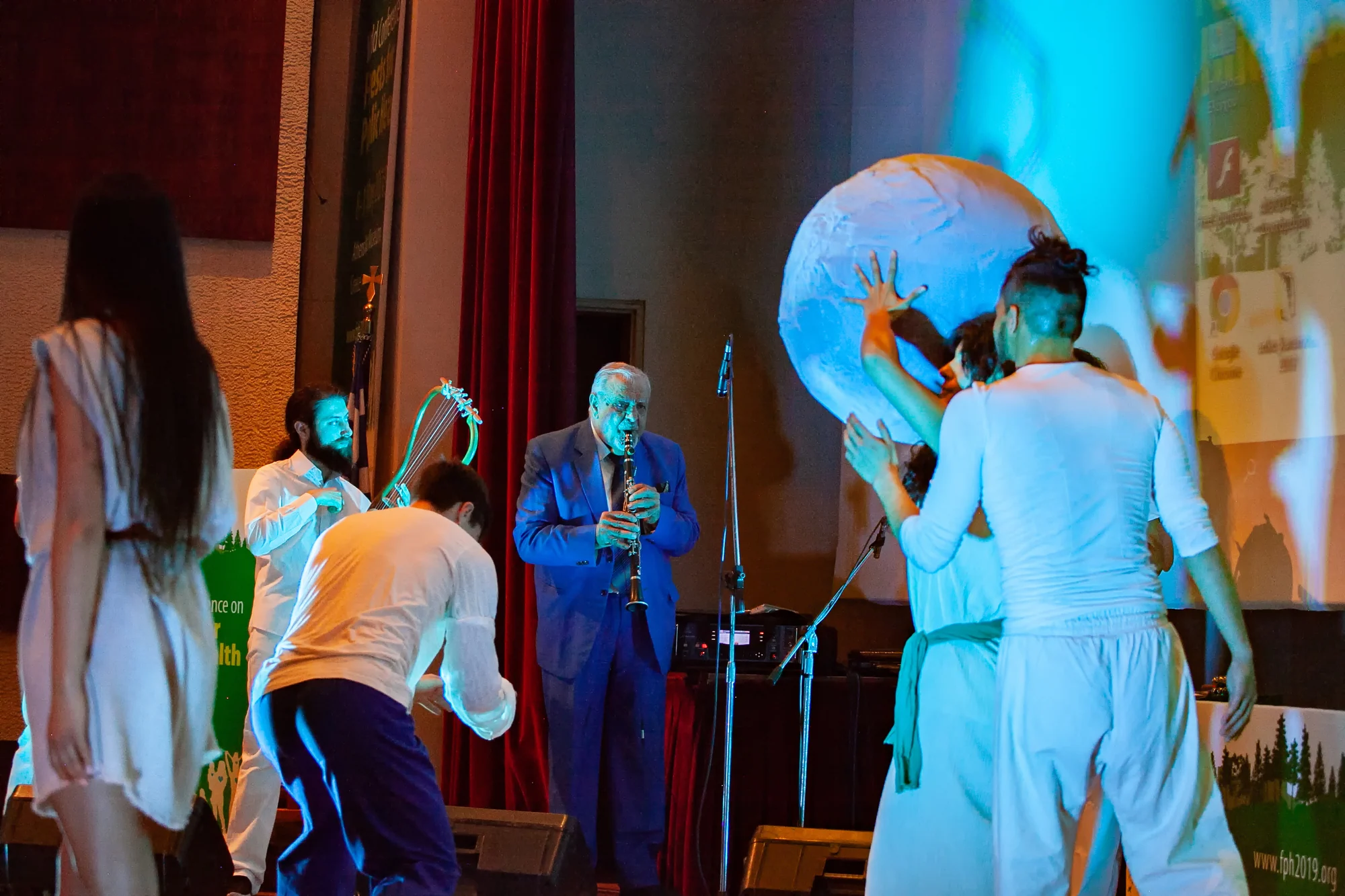 Dancers move around the globe beside musicians playing lyre and clarinet at the conference.