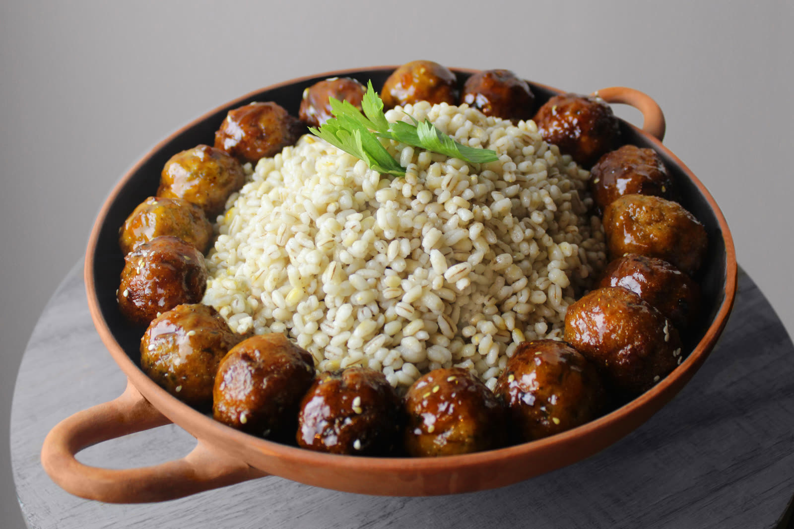 Barley surrounded by glazed savoury bites in a terracotta serving dish