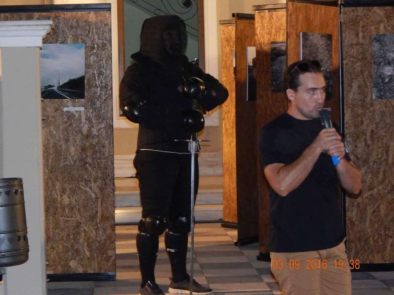 Georgios Katsos presents Byzantine swordsmanship | Via Egnatia Festival, Alexandroupolis, 2016 Georgios Katsos speaking into a microphone about Byzantine swordsmanship beside an interpreter in black protective armour at the Via Egnatia Festival in Alexandroupolis