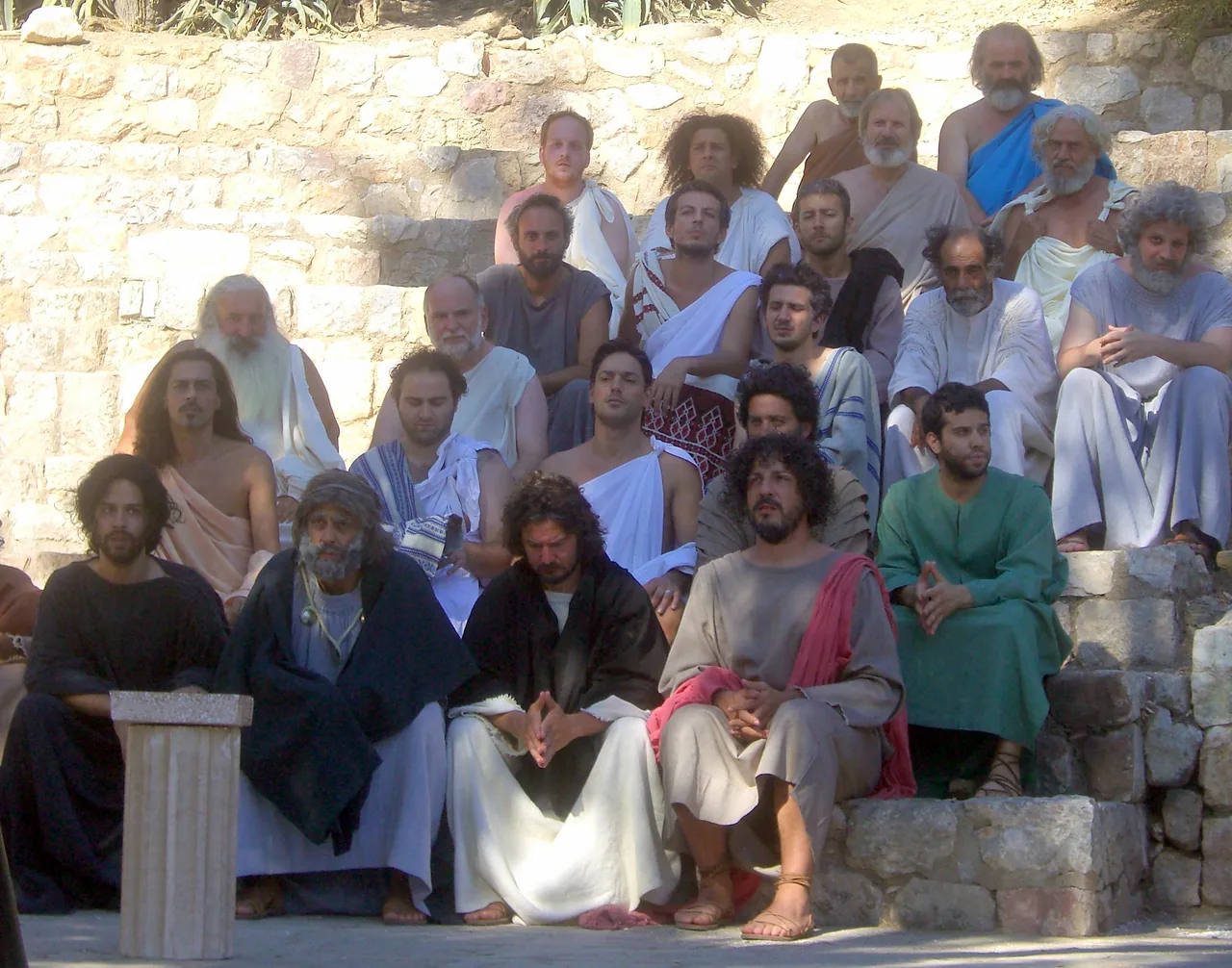 Group in draped ancient Greek-inspired garments and sandals seated on stone tiers outdoors