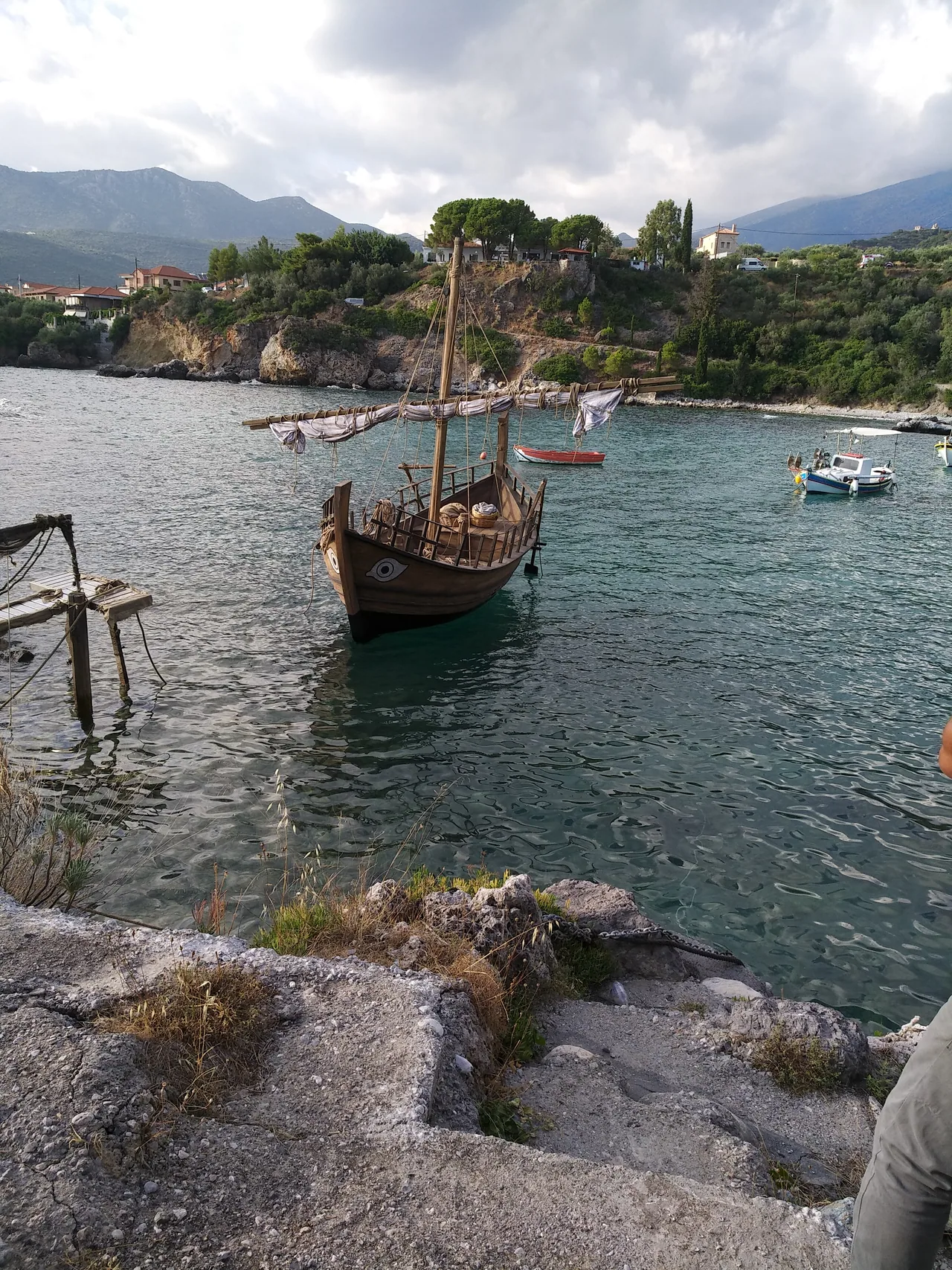Reconstructed wooden sailing vessel with painted bow eyes, mast and furled sail moored in a coastal inlet